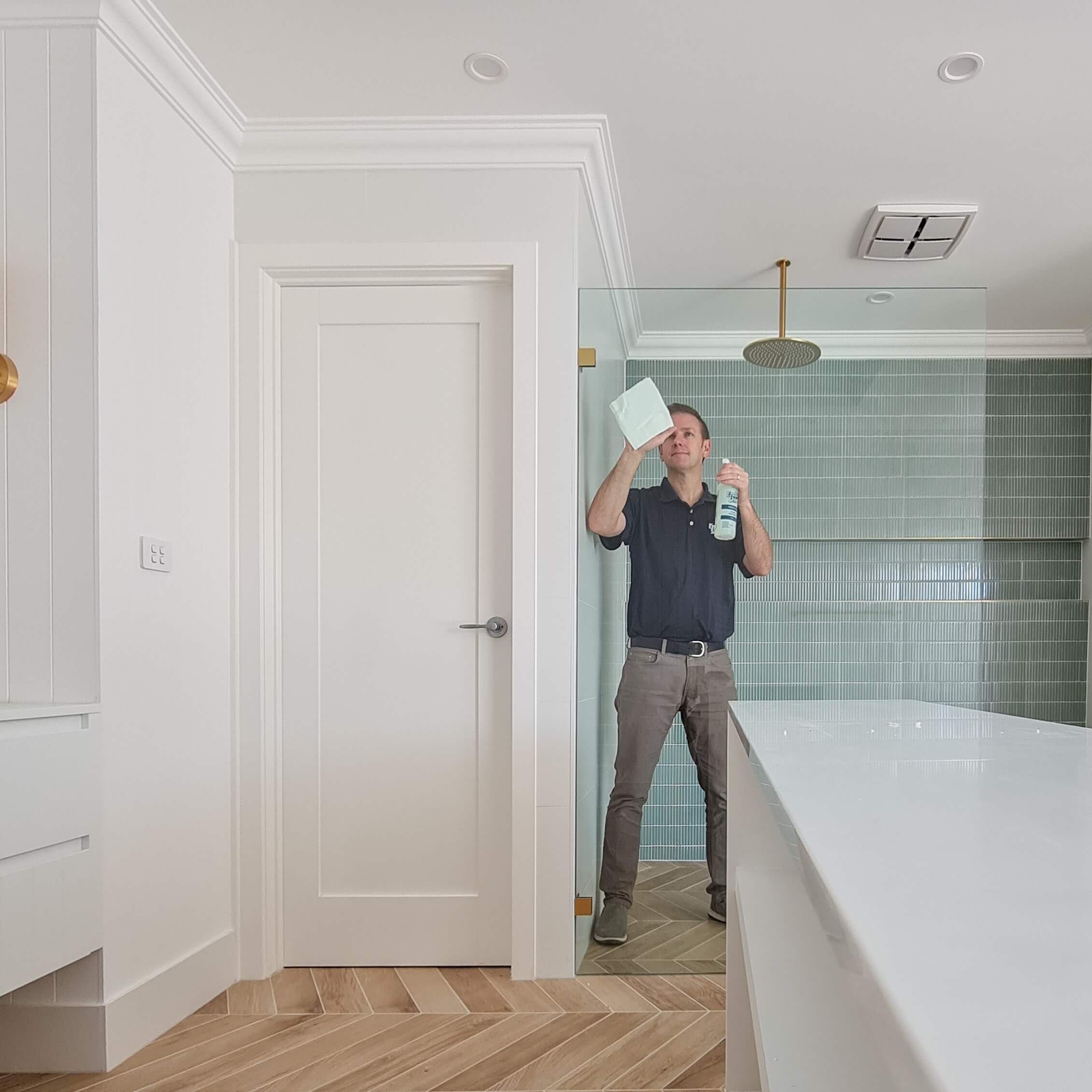 man applying enduroshield glass treatment to shower glass with spray bottle and white cloth